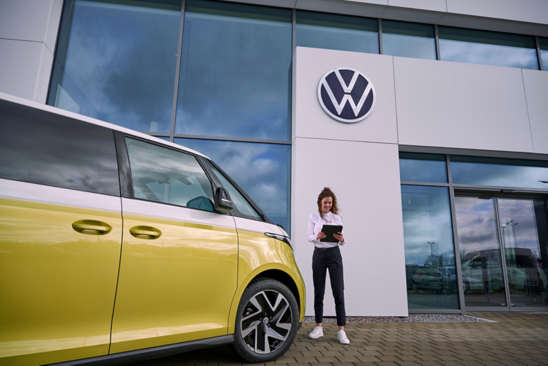 Pracownica serwisu obok Volkswagena ID. Buzz przed budynkiem salonu.