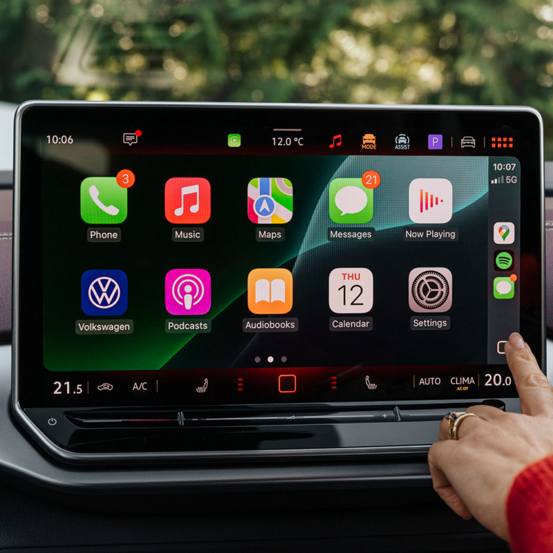 Close up image of person with one hand on steering wheel and other hand on digital display