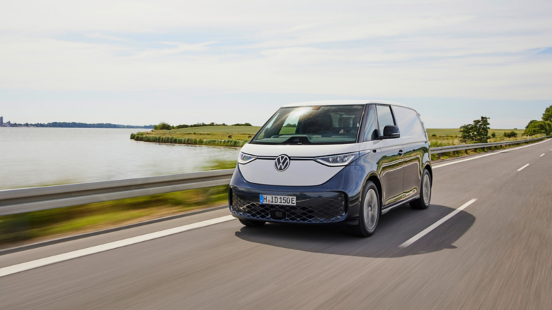 Tvåtonslackerad VW ID. Buzz Cargo elskåpbil kör på en väg med vatten i bakgrunden