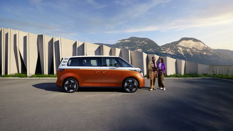 ID. Buzz People orange et blanc stationné sur un parking devant une montagne.