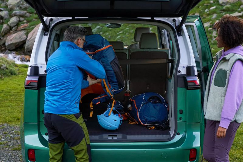 Een vrouw en man laden iets achterin een Volkswagen ID. Buzz. Op de achtergrond natuurrijk gebied.