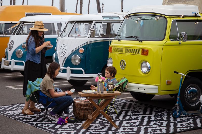 Eine Familie macht Picknick vor parkenden VW Bullis.