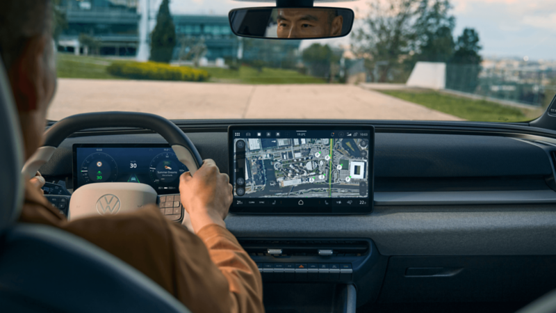An over-the-shoulder shot of a man driving a VW ID. Cross down a road.