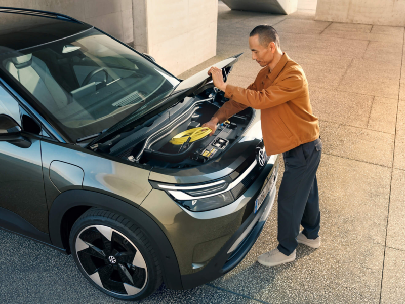 A man is opening the bonnet of a VW ID. Cross and reaching for the charging cables.