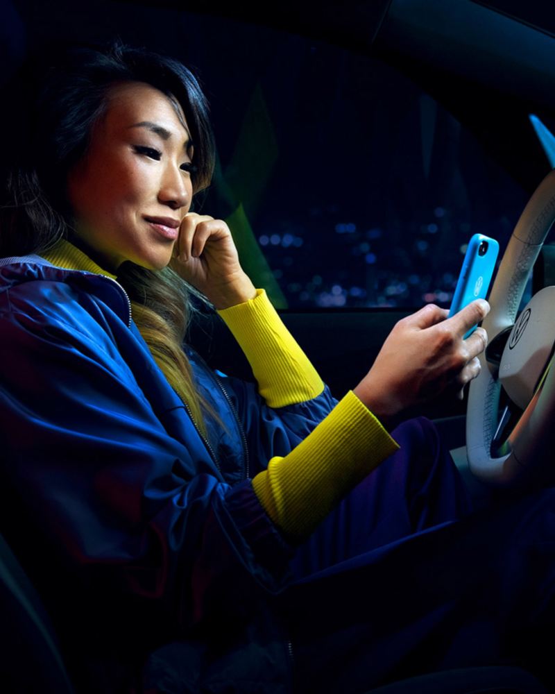 VW ID Cockpit. Frau sitzt auf Fahrersitz und schaut auf Smartphone.