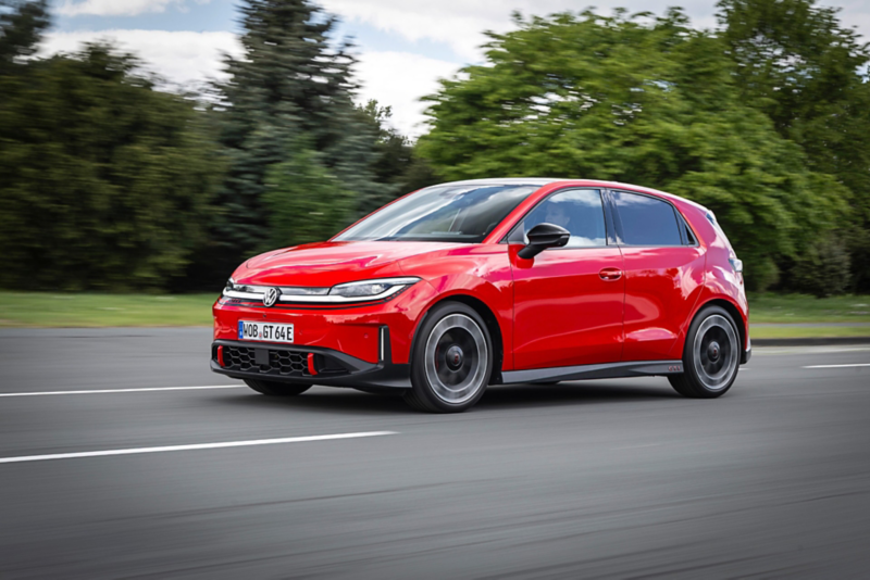 A red Volkswagen ID. Polo GTI electric hatchback driving fast on an open road, with a motion blur effect on the ground and green trees in the background.
