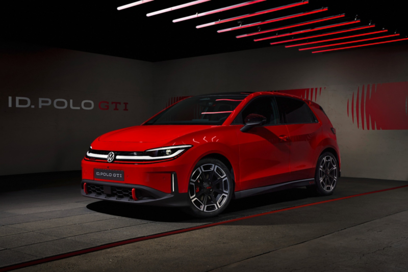 Front three-quarter view of a red Volkswagen ID. Polo GTI electric hatchback parked in a dimly lit studio with linear red ceiling lights.