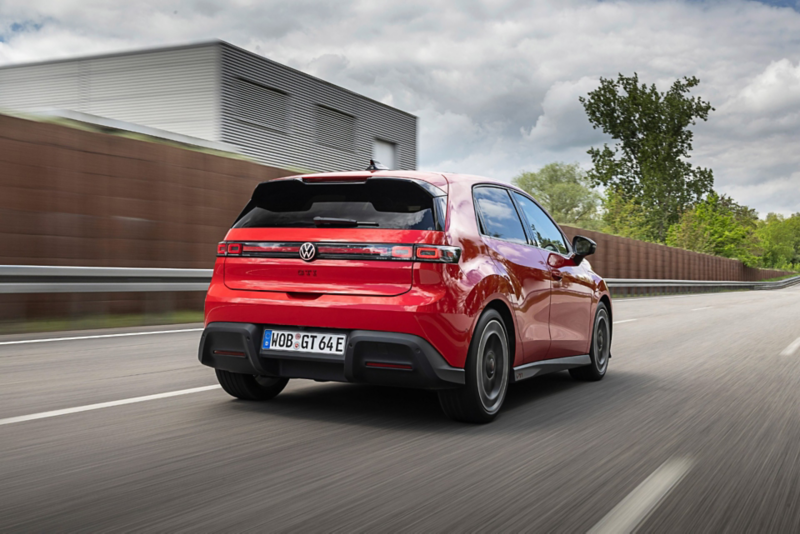 Rear three-quarter view of a red Volkswagen ID. Polo GTI electric hatchback driving on a highway, featuring a sleek rear spoiler and modern taillight design.