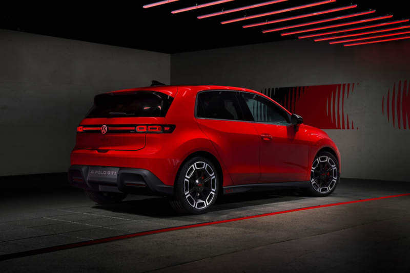 Rear three-quarter view of a red Volkswagen ID. Polo GTI electric car parked in a dark studio under red neon ceiling lights, showcasing its sharp taillights and sporty wheels.