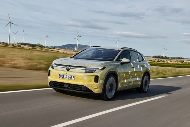 A yellow ID. Tiguan driving down a country road with wind turbines in the background..