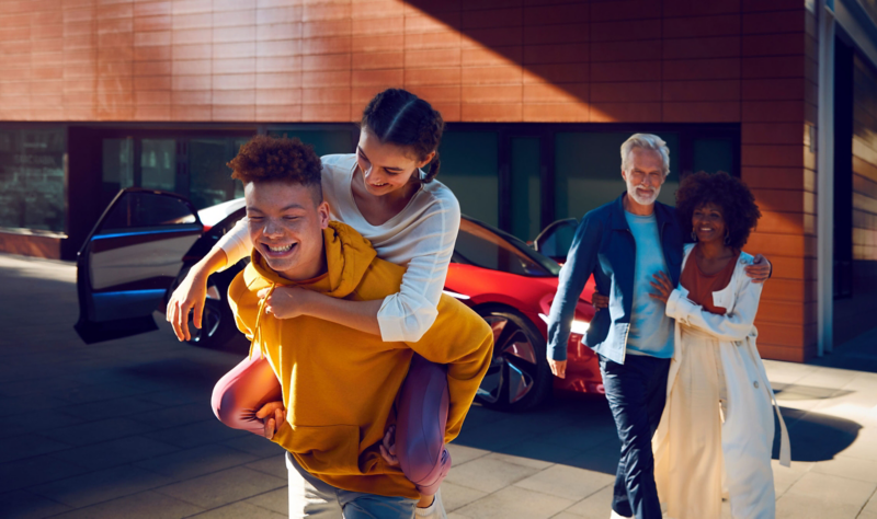 Four people standing in front of a red ID. Vizzion parked on the street, laughing together.