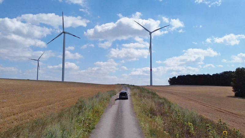 ID.3 fährt auf einen Feld weg und 3 Windmühle im Hintergrund
