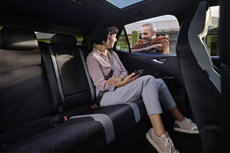 Interieur shot van de Volkswagen ID.3, focus ligt op de achterbank waar een meisje zit, een man kijkt naar haar vanaf buiten en leunt tegen de auto