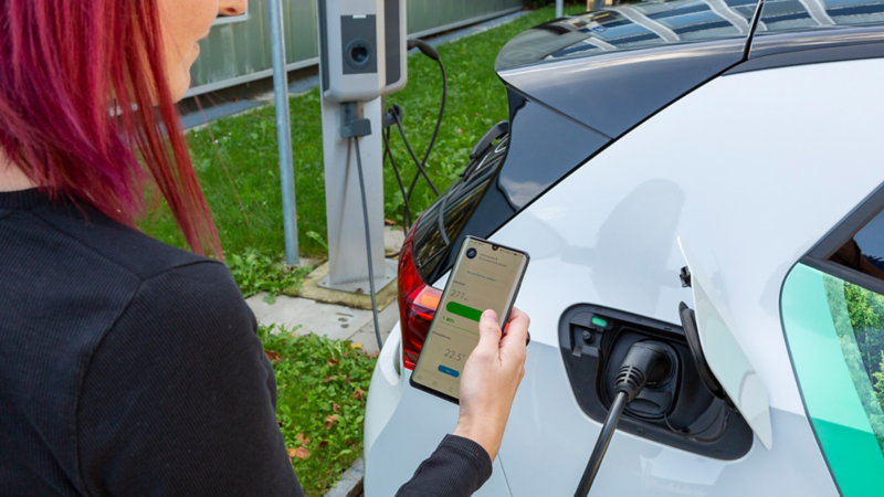 ID.3 ist gerade am Laden und eien Frau schaut aufs Smartphone auf dem die We Connect App ersichtlich ist