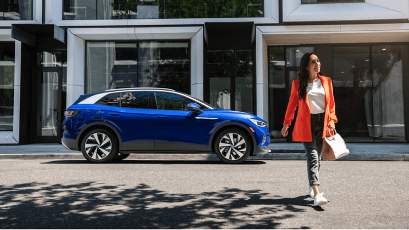 A woman walking on the street while the 2022 Volkswagen ID.4 parked next to the office building