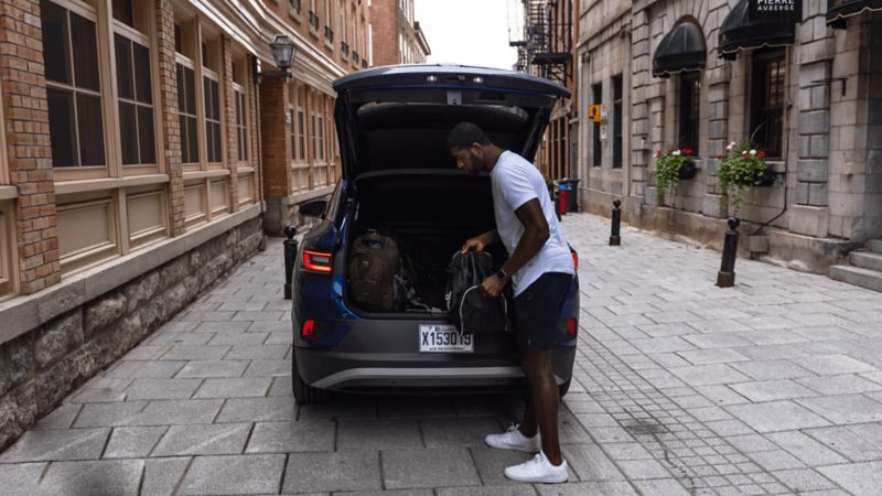 Un homme met des sacs dans le coffre d’un ID.4 2021 de Volkswagen stationné dans la rue.