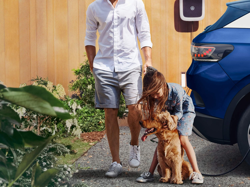 A man and a child with a dog walking towards a parked ID.4