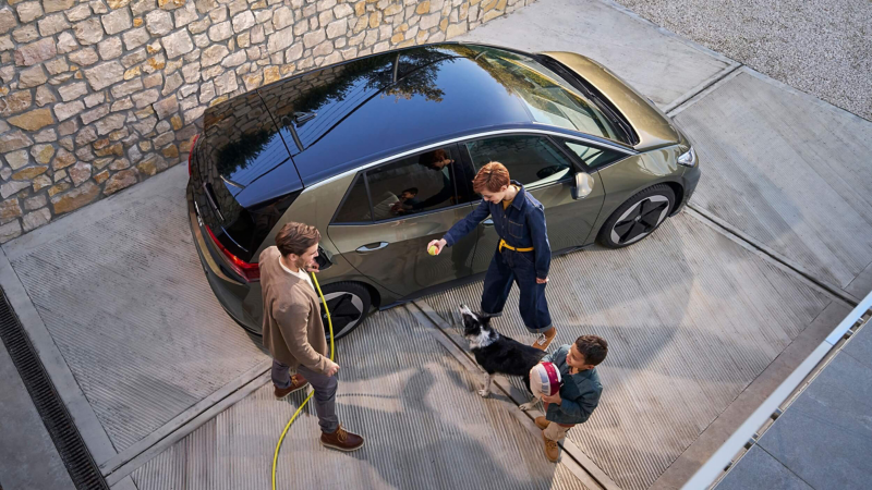 A man charging an ID.3 with 2 children and a dog playing next to the car