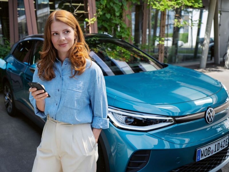 A woman holding a phone and leaning on a VW ID.4