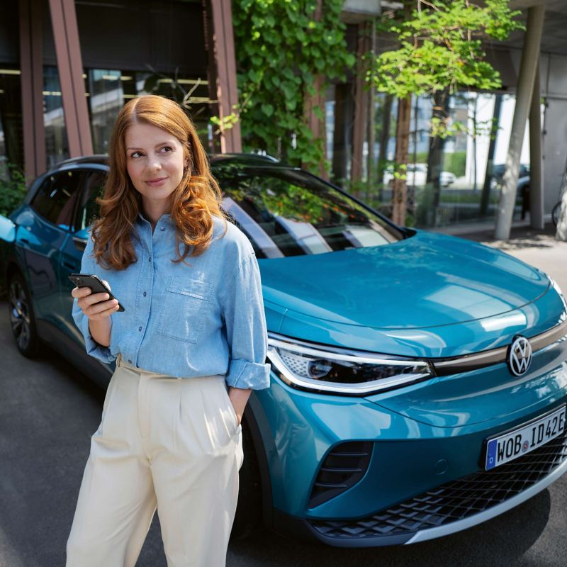 A woman holding a phone and leaning on a VW ID.4