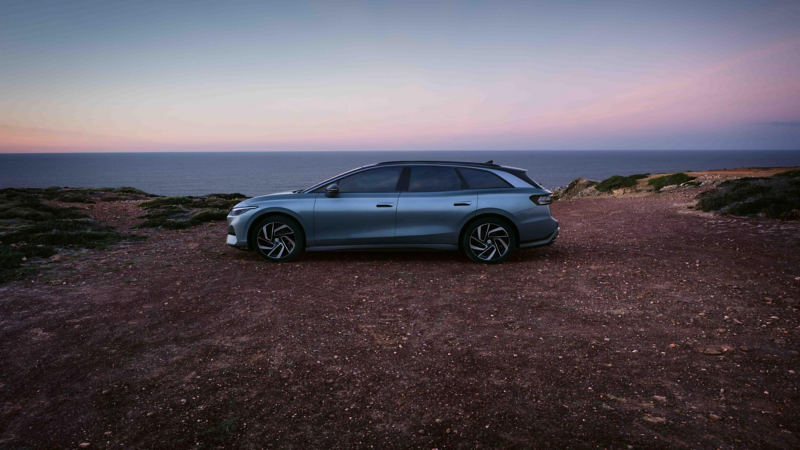 Side view of an ID.7 Tourer parked on a graveled road with coastal waters in the background