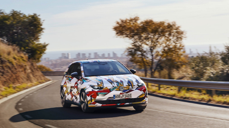 Volkswagen ID. Polo mit grafischer Folierung fährt auf einer kurvigen Strasse mit Stadtblick im Hintergrund.