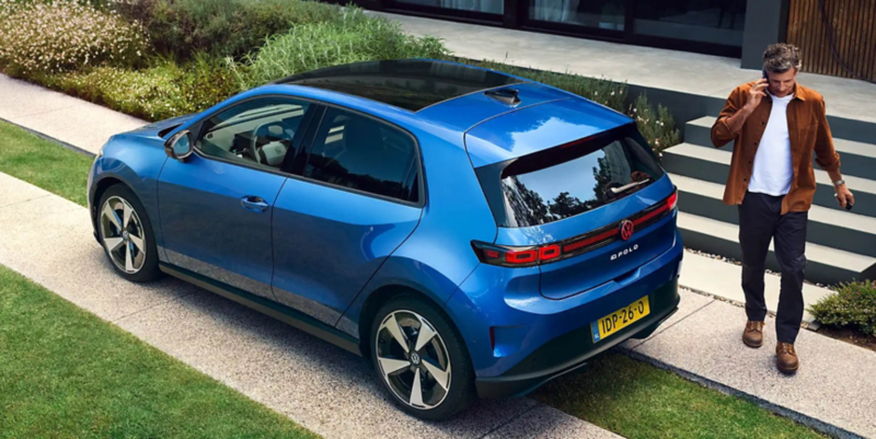 A woman is sitting in the driver's seat of a blue VW ID. Polo and reaches for a bouquet of flowers on the passenger seat.