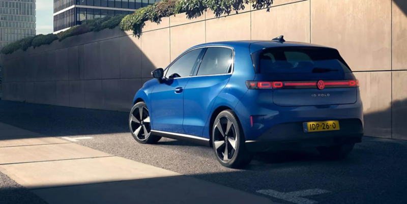 A blue VW ID. Polo is standing on the roadside in front of a green wall, a man is walking towards it.