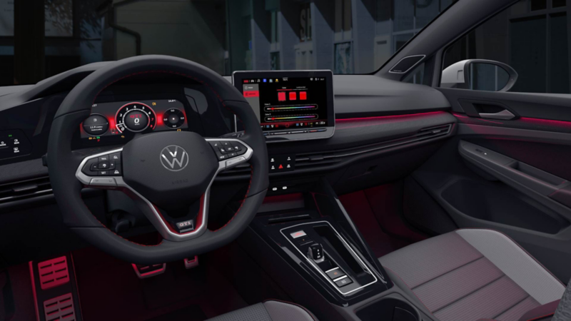 Interior de Nuevo GTI 2025 con iluminación ambiental en color rojo y pantalla de 12 pulgadas. 