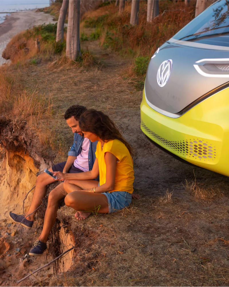 Couple sitting by electric vehicle looking at ocean.