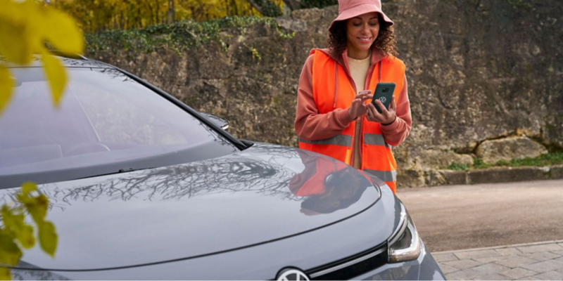 Mujer pidiendo asistencia en carretera cerca de un vehículo VW.