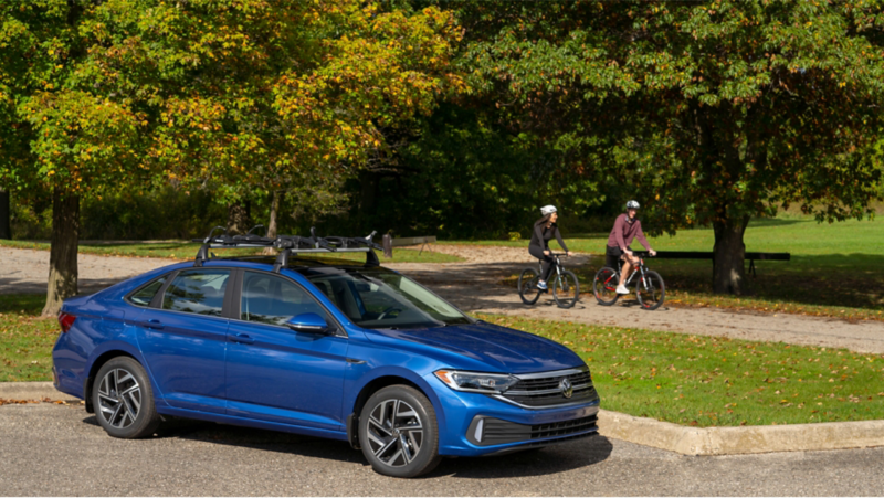 Motociclistas pasando junto a un VW Jetta en un parque.