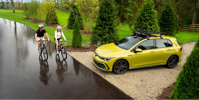 Bikers riding past a VW GTI in a park.