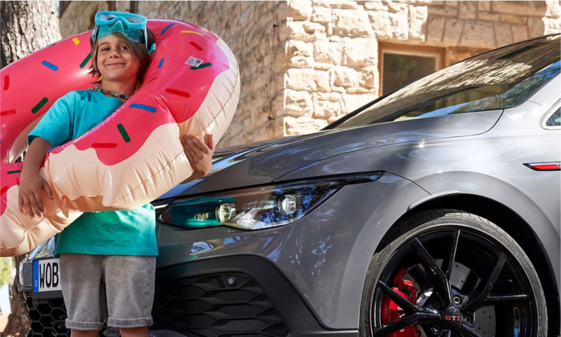 Young girl with inflatable pool toy standing near VW GTI.