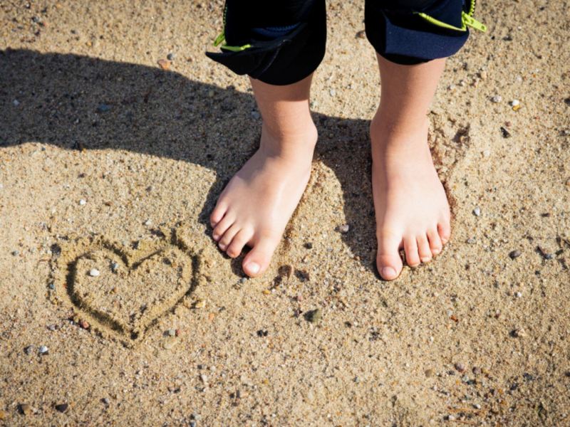 Person's feet on beach with a heart drawn in sand.