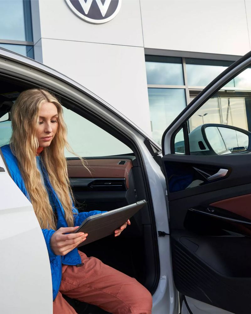 Mujer sentada en un vehículo VW revisando el reporte de cobertura sin preocupaciones.