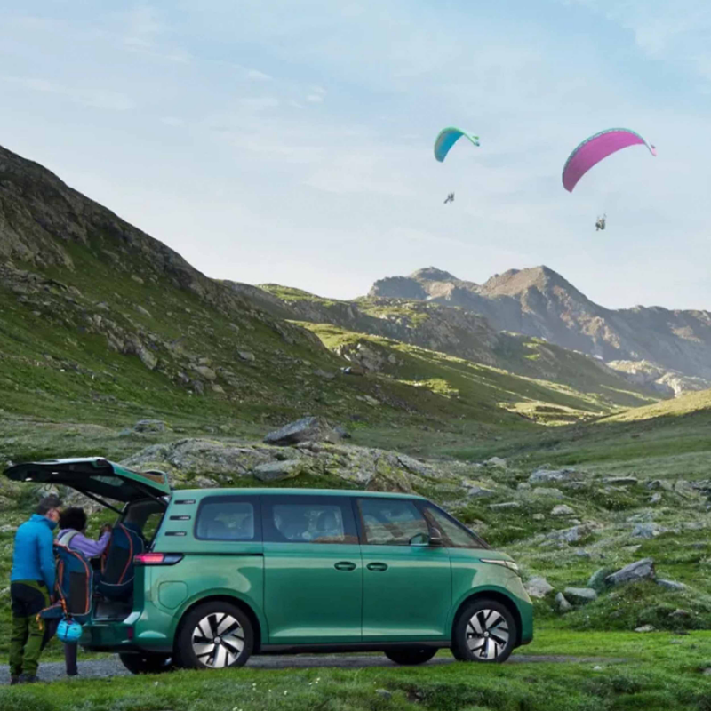 an EV VW van on a mountain looking out at paragliders in the sky