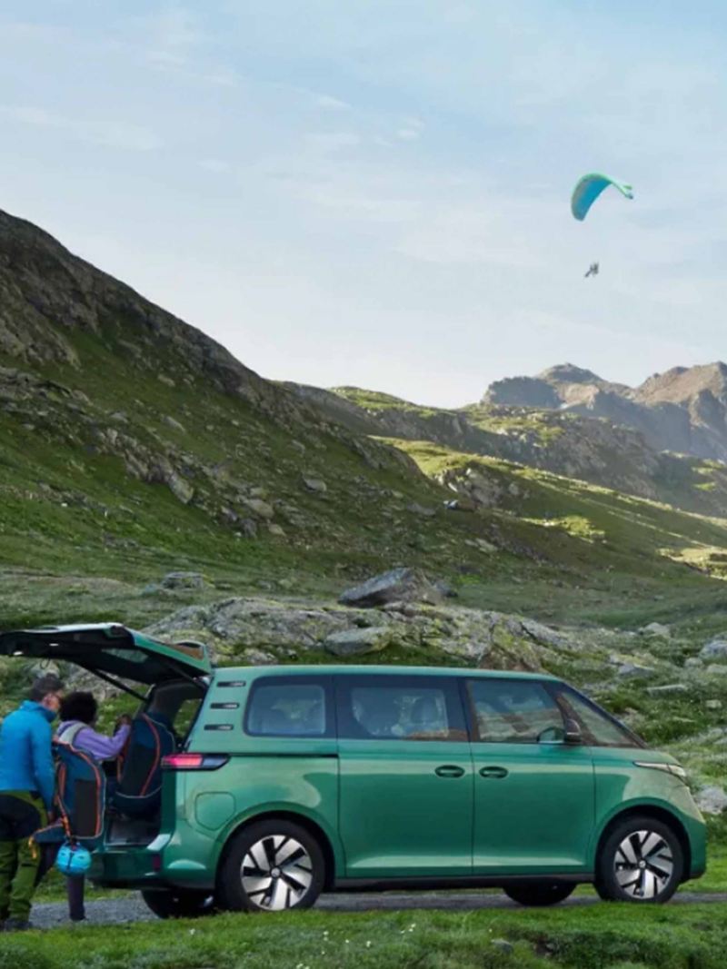 an EV VW van on a mountain looking out at paragliders in the sky