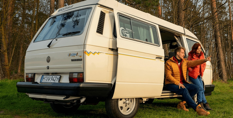 Mężczyzna i kobieta w otwartych drzwiach starszej generacji Volkswagena California.