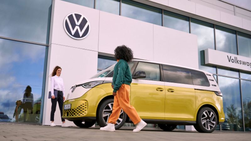 a woman walking towards a VW expert and a yellow ID.buzz outside a retailers 