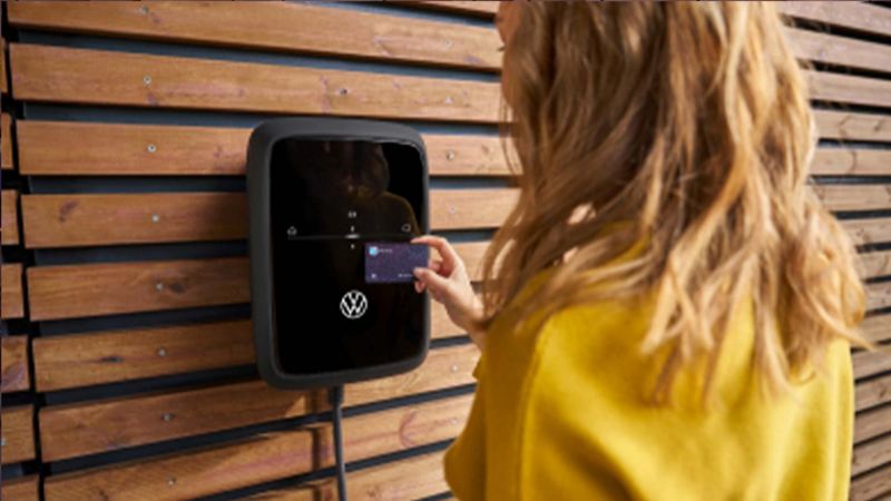 A woman tapping her credit card against the NFC reaser on a VW charging station. 