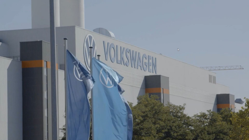 Fahnen mit Volkswagen Logo vor einer großen Produktionshalle