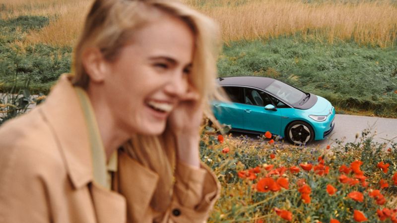 I förgrunden syns en skrattande kvinna, i bakgrunden en VW ID.3.