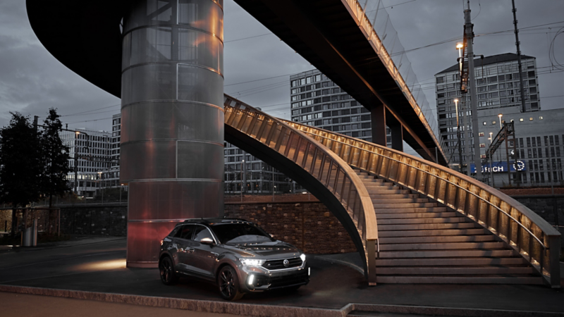 Dans la lumière du soir, le T-Roc R avec feux garé à côté d'un escalier en colimaçon.