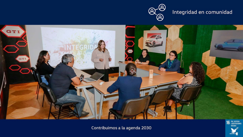Colaboradores en taller de integridad con imágenes de autos Volkswagen al fondo.