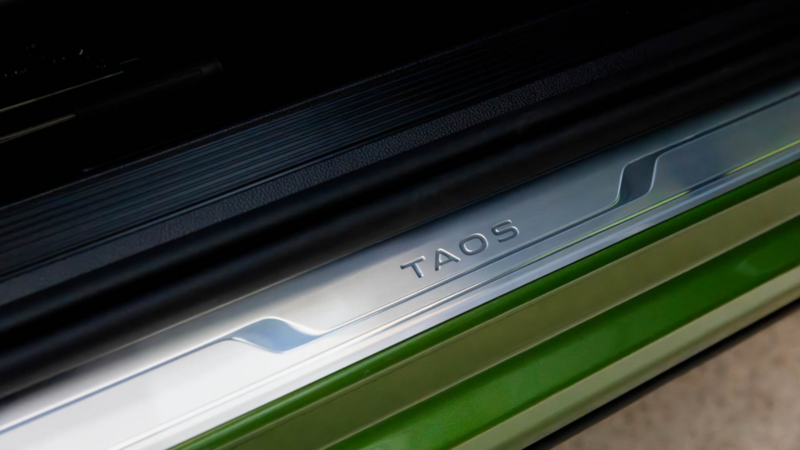 Estribo metálico de un Volkswagen verde con la inscripción Taos iluminada, visto en primer plano.