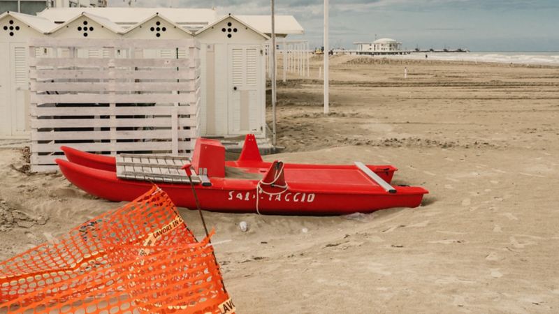 Ein rotes Boot, welches am Sandstrand liegt.