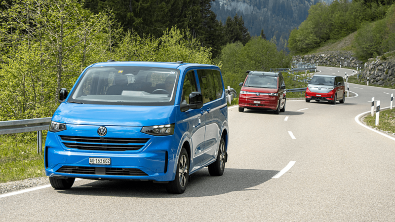 Trois modèles VW Bus roulent sur une route de montagne sinueuse dans les Alpes.