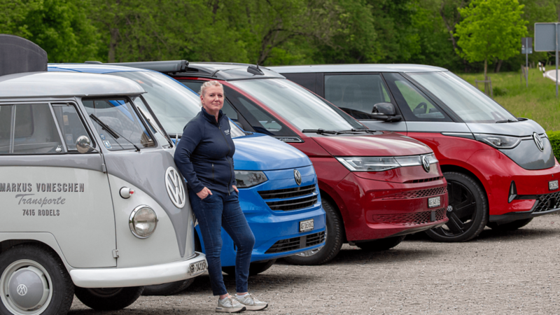 Eine Frau steht vor vier VW Bus Generationen – vom T1 bis zum ID. Buzz.