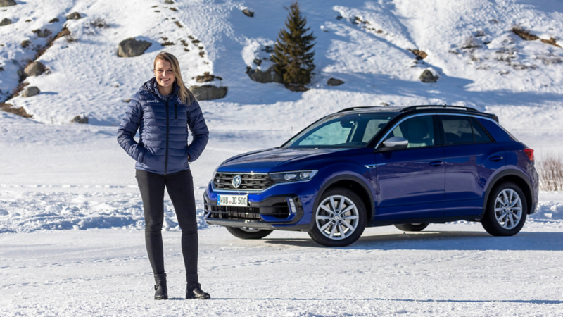 Rennfahrerin posiert vor blauen T-Roc R im Schnee.